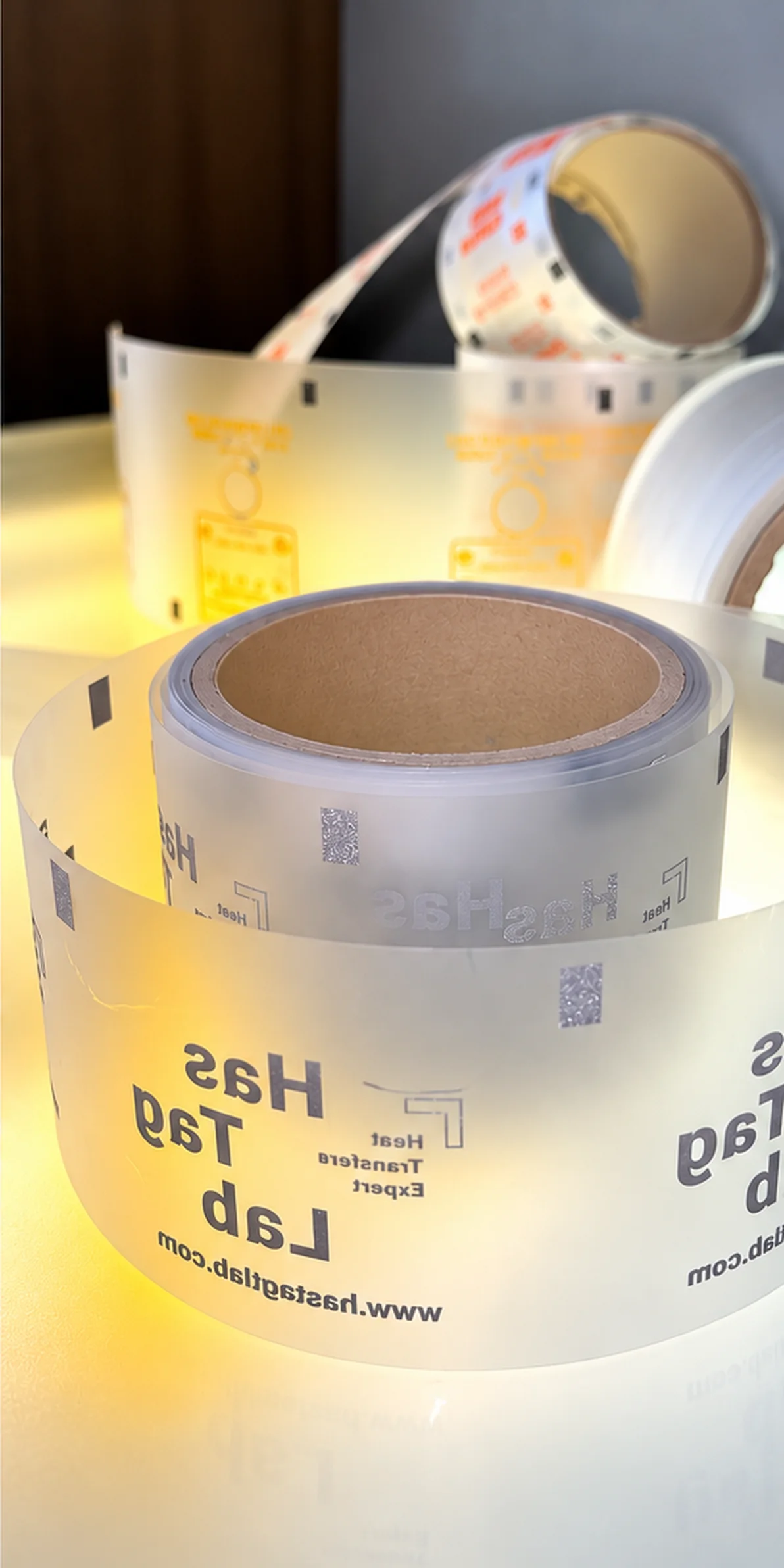 Roll of clear HasTagLab heat transfer labels on a lit worktable